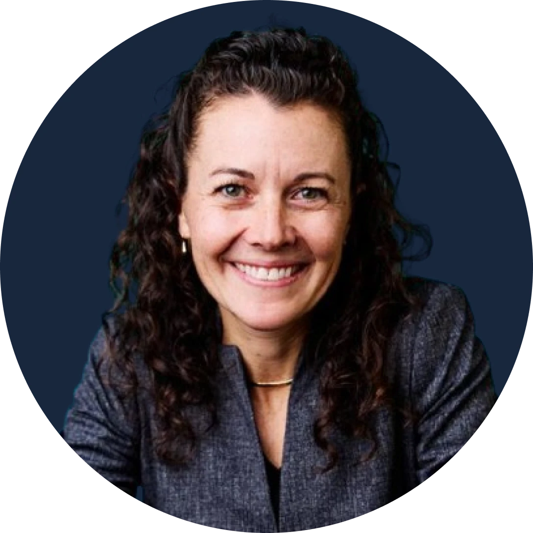 smiling woman with curly dark hair wearing a gray blazer posed against a dark blue circular background